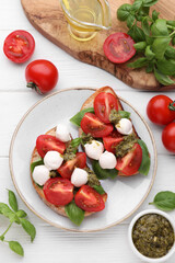 Delicious Caprese sandwiches with mozzarella, tomatoes, basil and pesto sauce on white wooden table, flat lay