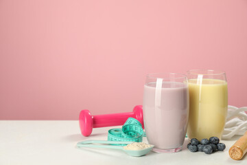 Tasty shakes with blueberries, sports equipment, measuring tape and powder on white table against...