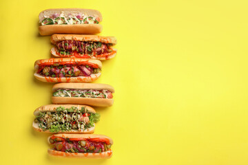 Delicious hot dogs with different toppings on yellow background, flat lay. Space for text