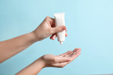 Woman applying cosmetic cream from tube onto her hand on light blue background, closeup