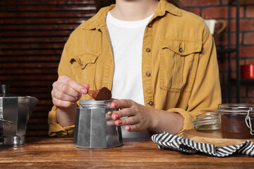 Woman putting ground coffee into moka pot at wooden table, closeup