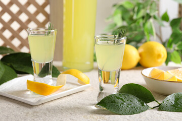 Tasty limoncello liqueur and green leaves on light textured table