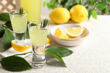 Tasty limoncello liqueur, lemons and green leaves on white textured table, closeup. Space for text
