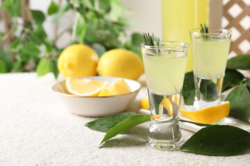 Tasty limoncello liqueur, lemons and green leaves on white textured table, closeup. Space for text