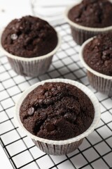 Tasty chocolate muffins and cooling rack on white table, closeup