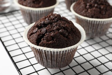 Tasty chocolate muffins and cooling rack on white table, closeup