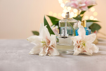 Fototapeta na wymiar Bottles of perfume and beautiful lily flowers on table against beige background with blurred lights, closeup. Space for text