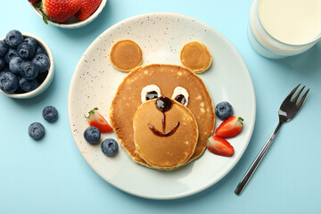 Creative serving for kids. Plate with cute bear made of pancakes and berries on light blue table, flat lay