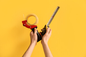 Worker with adhesive and measure tapes on yellow background