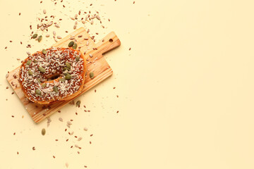 Wooden board of tasty bagel with sesame and pumpkin seeds on beige background