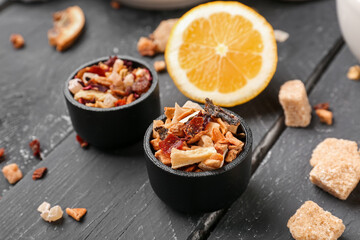 Bowls with dried fruit tea on black wooden table, closeup
