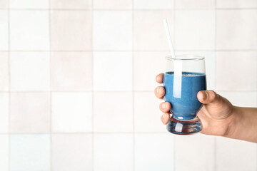 Female hand with glass of blue smoothie on white background