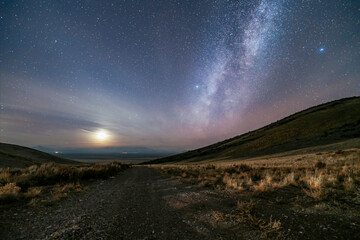 The moon and Milky Way over a grassland landscape