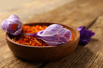 Bowl of dried saffron threads with crocus flowers on wooden table