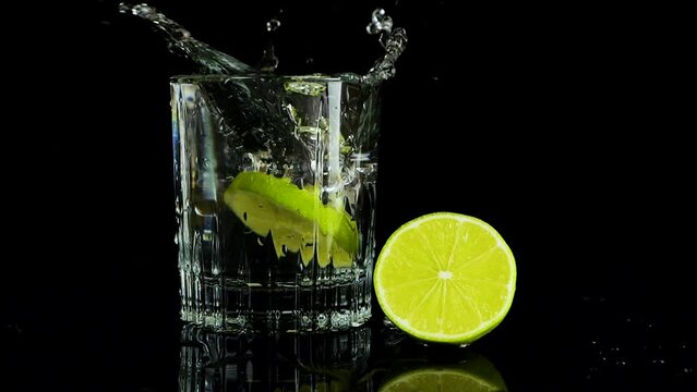 A slice of lime falls into a glass of water. Slow motion. Isolated on black background.