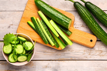 Board with fresh cut cucumber on light wooden background