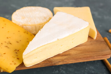 Wooden board with pieces of tasty cheese on table, closeup