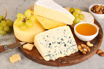 Plate with different types of cheese, honey and grapes on grunge background