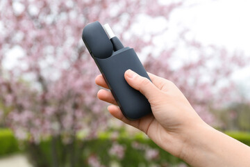 Female hand holding modern electronic cigar outdoors