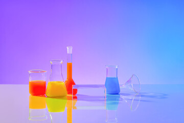 Front view of colorful liquids inside transparent laboratory flasks on a blue-purple gradient background. A glass podium is placed in the center of the frame for display.