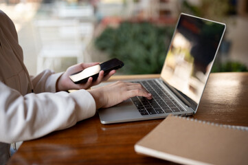 A woman in hoodie using her laptop computer at a table in a coffee shop, working remotely.