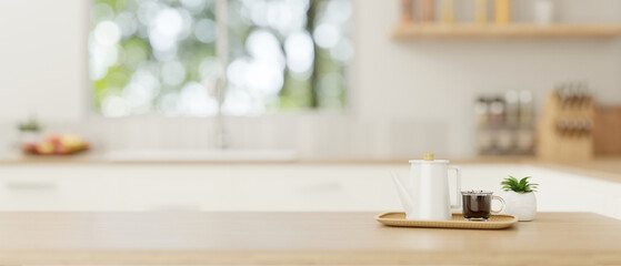 A copy space on a wooden tabletop with a coffee pot and a coffee cup in a minimal bright kitchen.