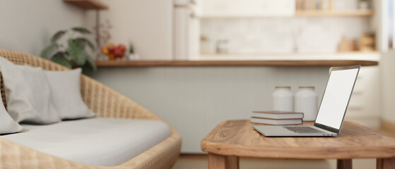 A laptop on a hardwood coffee table in a cosy Scandinavian living room with a cosy wicker couch.