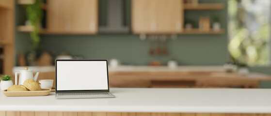 A white-screen laptop computer on a white kitchen tabletop in a modern green kitchen. Home workspace