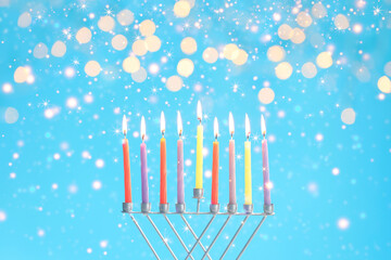 Hanukkah celebration. Menorah with burning candles on light blue background with blurred lights, closeup