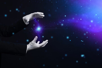 Magician in gloves showing trick on dark background, closeup. Space for text