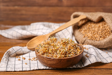 Bowl with sprouted wheat and spoon on wooden table