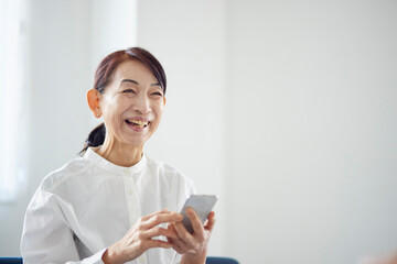リビングにてスマートフォンを使用する日本人のシニア女性
