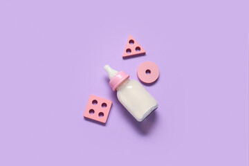 Bottle of milk for baby with toys on lilac background
