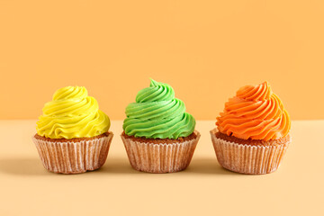 Tasty colorful cupcakes on orange background