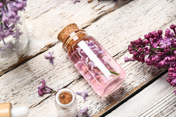 Bottle of lilac essential oil and flowers on light wooden background, closeup
