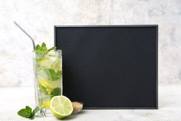 Glass of cold mojito and chalkboard on light background