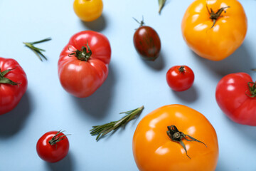 Different fresh tomatoes and rosemary on blue background