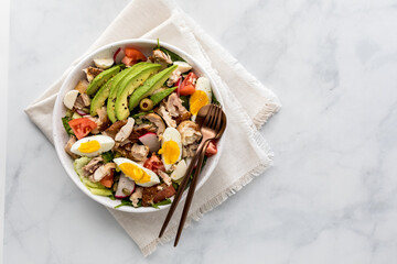 A healthy tossed salad with chicken, avocado and egg, ready for eating.