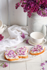 Plate of sandwiches with tasty cream cheese, lilac flowers and tea set on light tile table