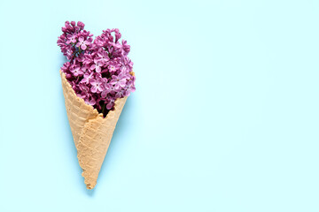 Waffle cone with beautiful lilac flowers on blue background