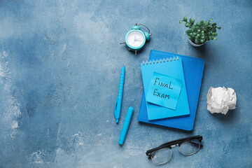 Notebooks with text FINAL EXAM, alarm clock and eyeglasses on grunge blue background