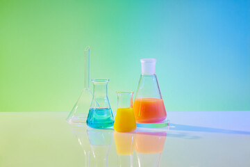 Front view of laboratory equipments - different size of erlenmeyer flasks filled color liquid, on green and blue gradient background. Concept: research, biochemistry, nature, pharmaceutical medicine
