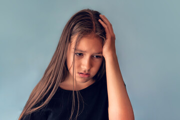 Closeup portrait stressed child, teenager girl hands on temples overwhelmed at school in life, blue background. Human facial expressions, emotions, feeling, perception