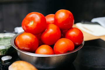 Ripe Whole Tomatoes in Metal Bowl. A bowl of bright red ripe tomatoes on a kitchen counter, ready for cooking or salad preparation.