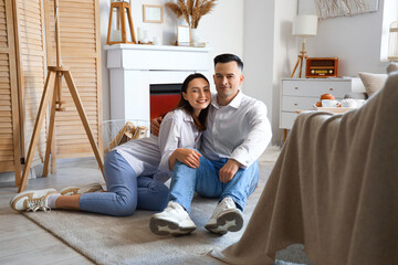 Young couple hugging near fireplace at home - obrazy, fototapety, plakaty