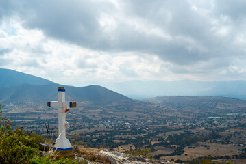 Paisaje. Cruz blanca cristiana sobre montaña. mirando al pueblo con montañas y cielo nublado de...