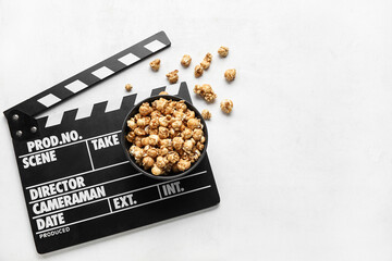 Bowl with tasty popcorn and clapperboard on white background
