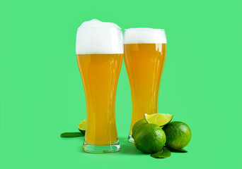 Glasses of cold beer with lime on green background