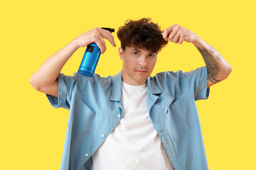 Handsome young man applying hair spray on his curly hair against yellow background