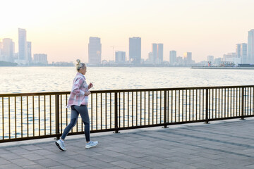 woman running on the promenade at sunrise. active city life, sport, healthy lifestyle. - obrazy, fototapety, plakaty